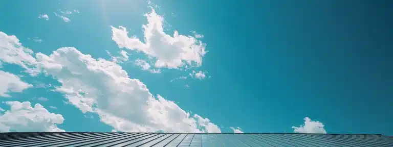 a skilled roofer positioning shiny steel sheets atop a newly constructed house under a bright blue sky.